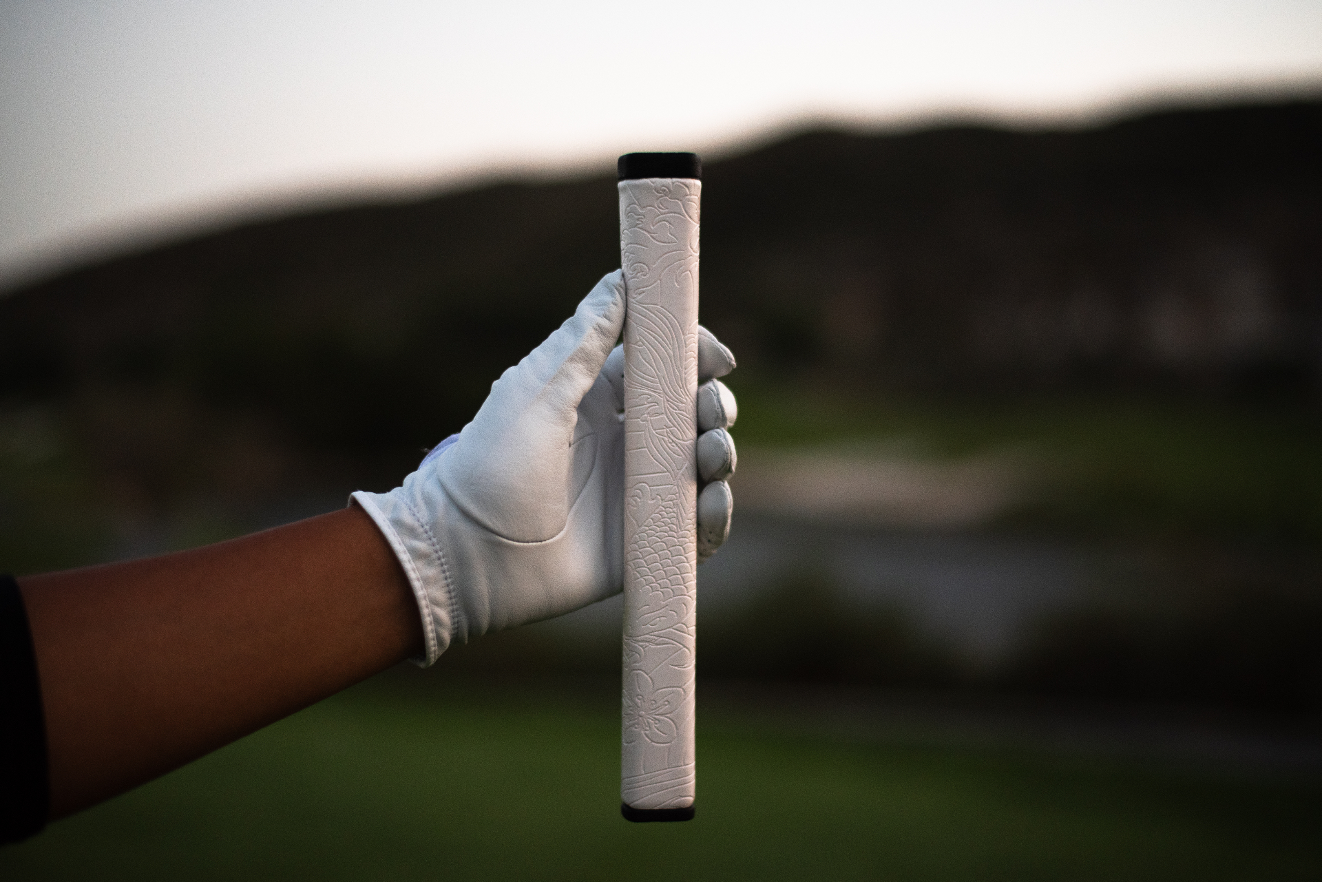 A gloved hand holding the Kaiyen putter grip on the course at golden hour